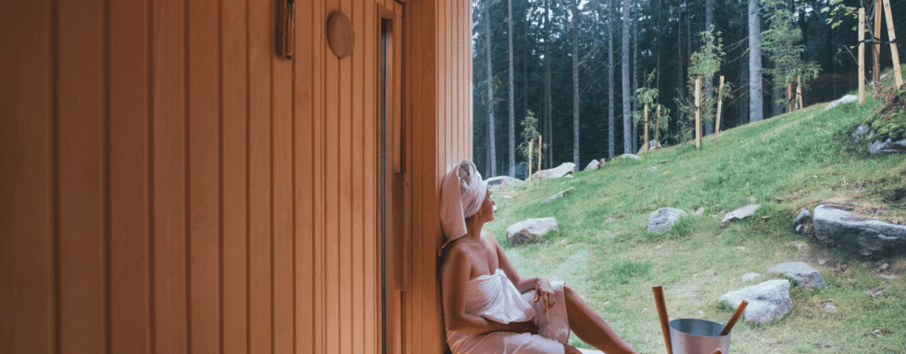 A woman relaxes on the edge of a wooden door in an outdoor sauna