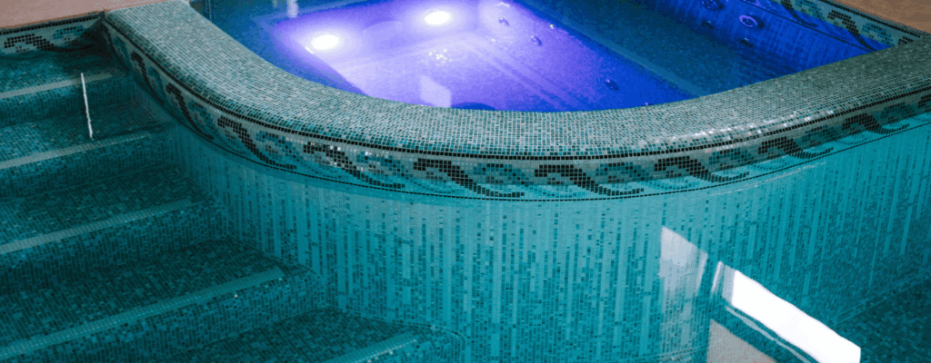 A bespoke hot tub sits in a blue-tiled pool area, showcasing its elegant design and inviting water.