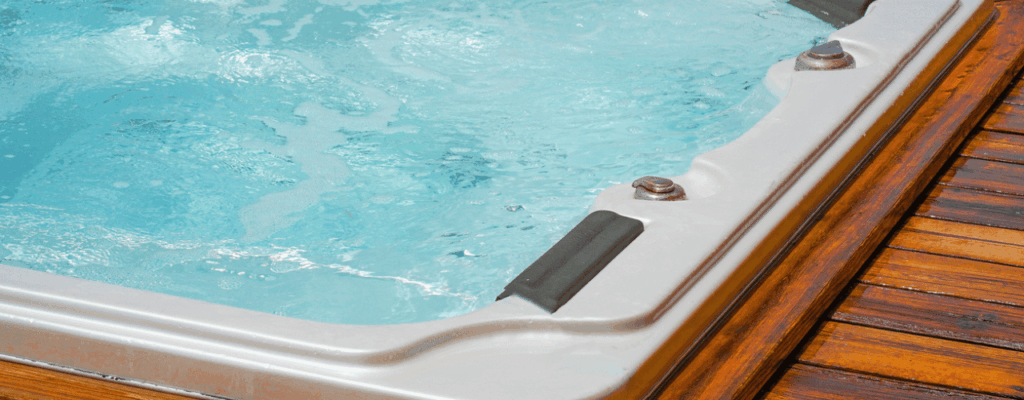 A jacuzzi swim spa situated on a wooden deck, surrounded by a serene outdoor environment.