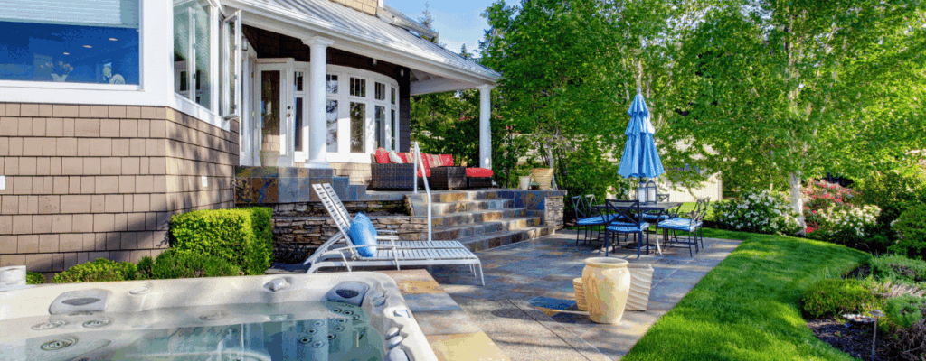 A serene backyard scene with a jacuzzi and comfortable patio seating amidst vibrant plants.